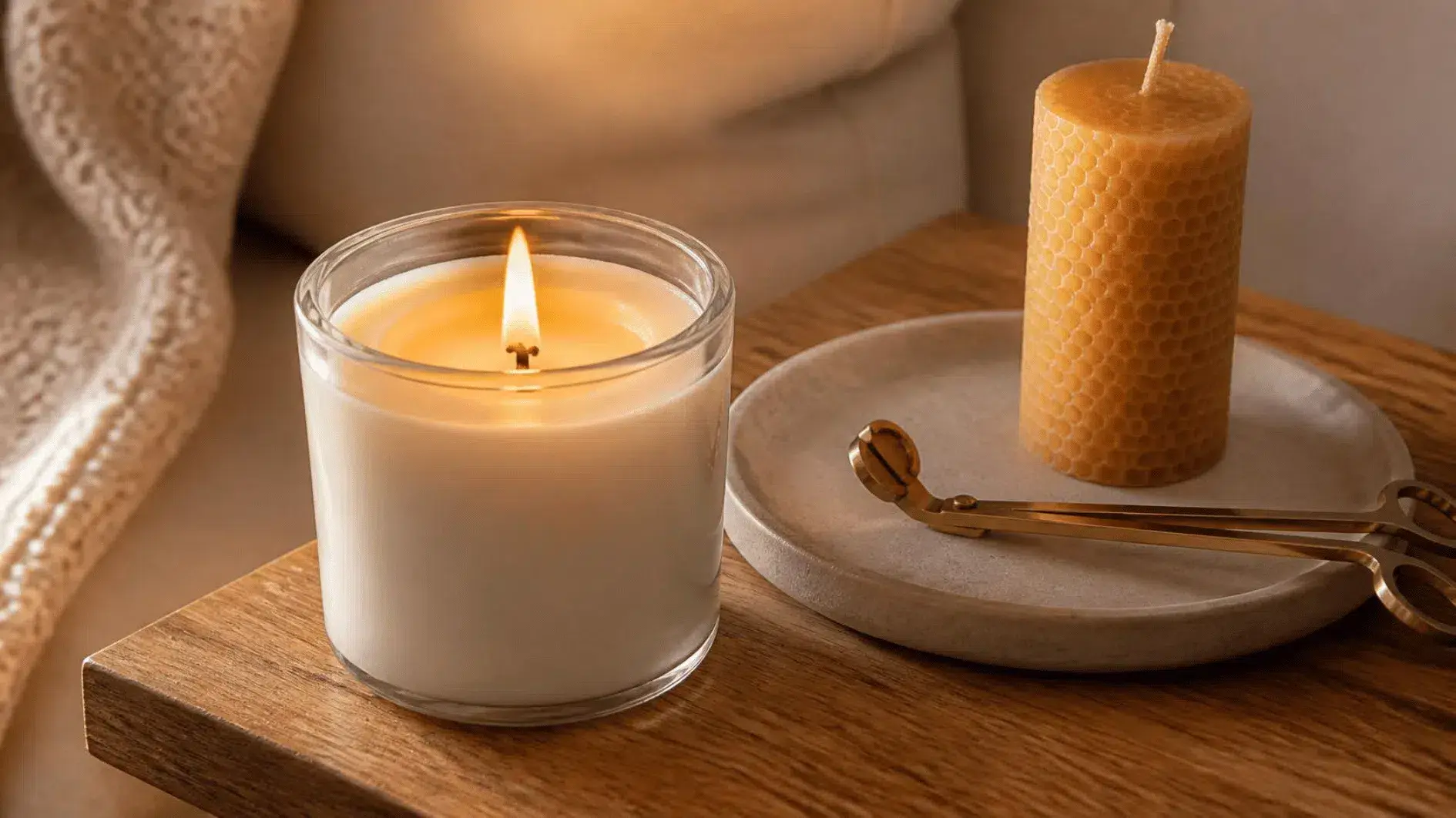 Lit soy wax candle in a glass jar with a full, even melt pool beside an unlit beeswax pillar candle and a brass wick trimmer on an oak tray